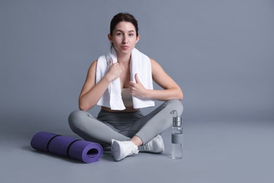 Photo of Woman in sportswear with bottle of water, fitness mat and towel on grey background