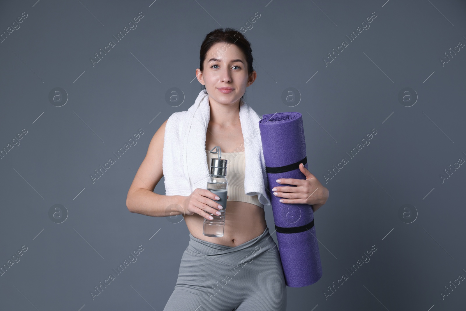 Photo of Woman in sportswear with bottle of water, fitness mat and towel on grey background