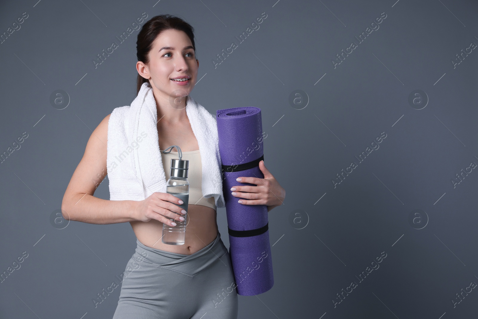 Photo of Woman in sportswear with bottle of water, fitness mat and towel on grey background, space for text