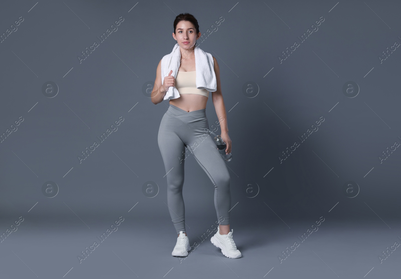 Photo of Woman in sportswear with bottle of water and towel on grey background