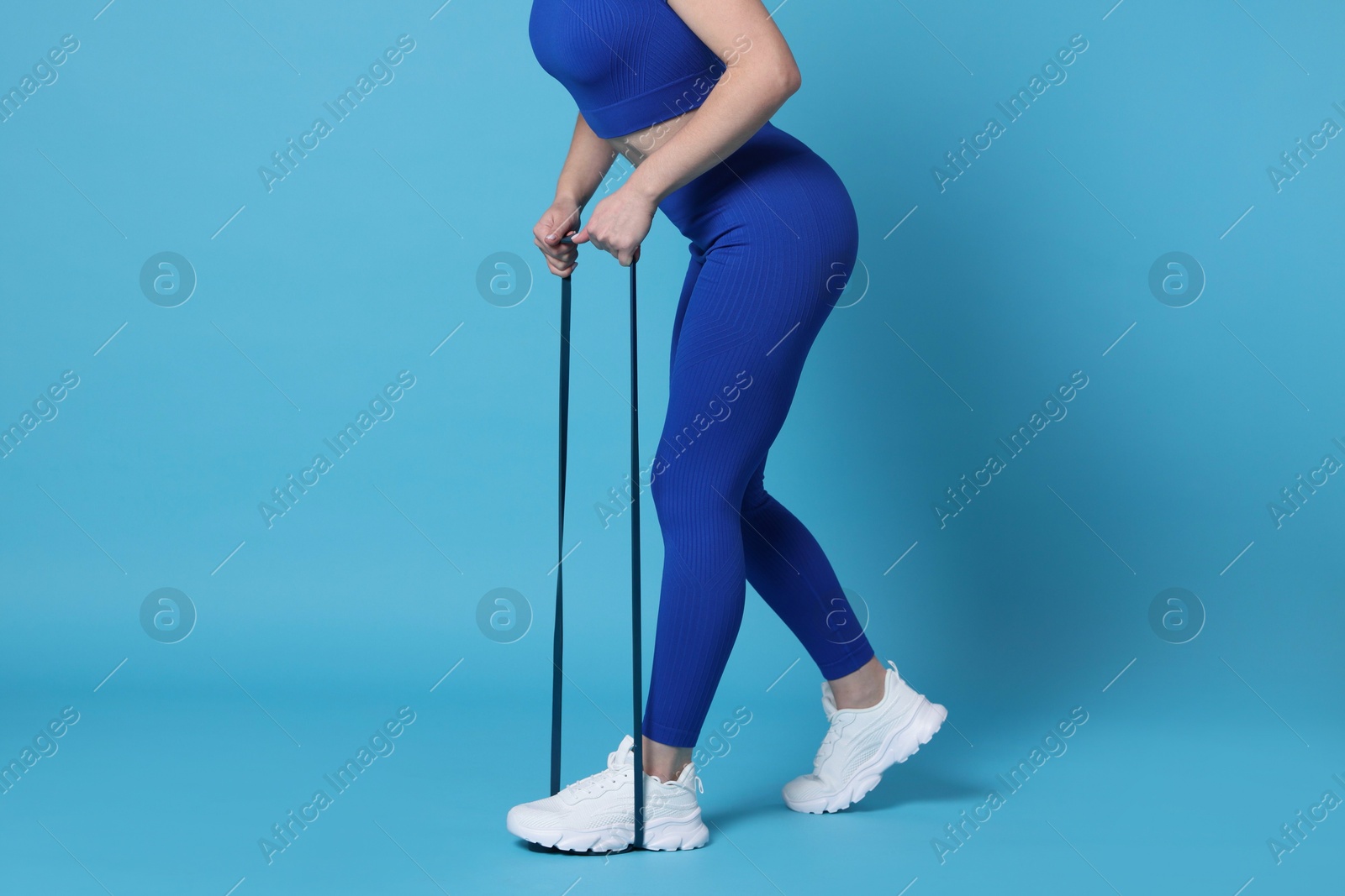 Photo of Woman in sportswear exercising elastic band on light blue background, closeup