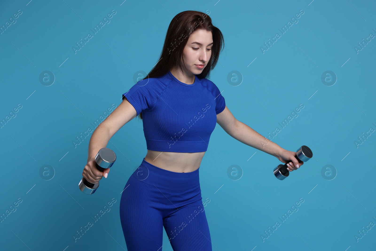 Photo of Woman in sportswear exercising with dumbbells on light blue background