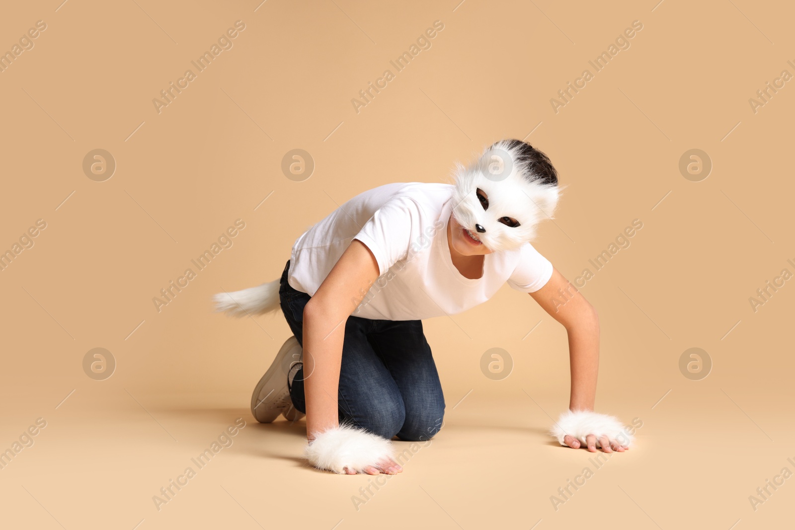 Photo of Quadrobics. Boy wearing cat mask, gloves and tail on beige background