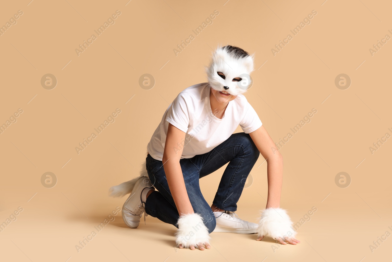 Photo of Quadrobics. Boy wearing cat mask, gloves and tail on beige background