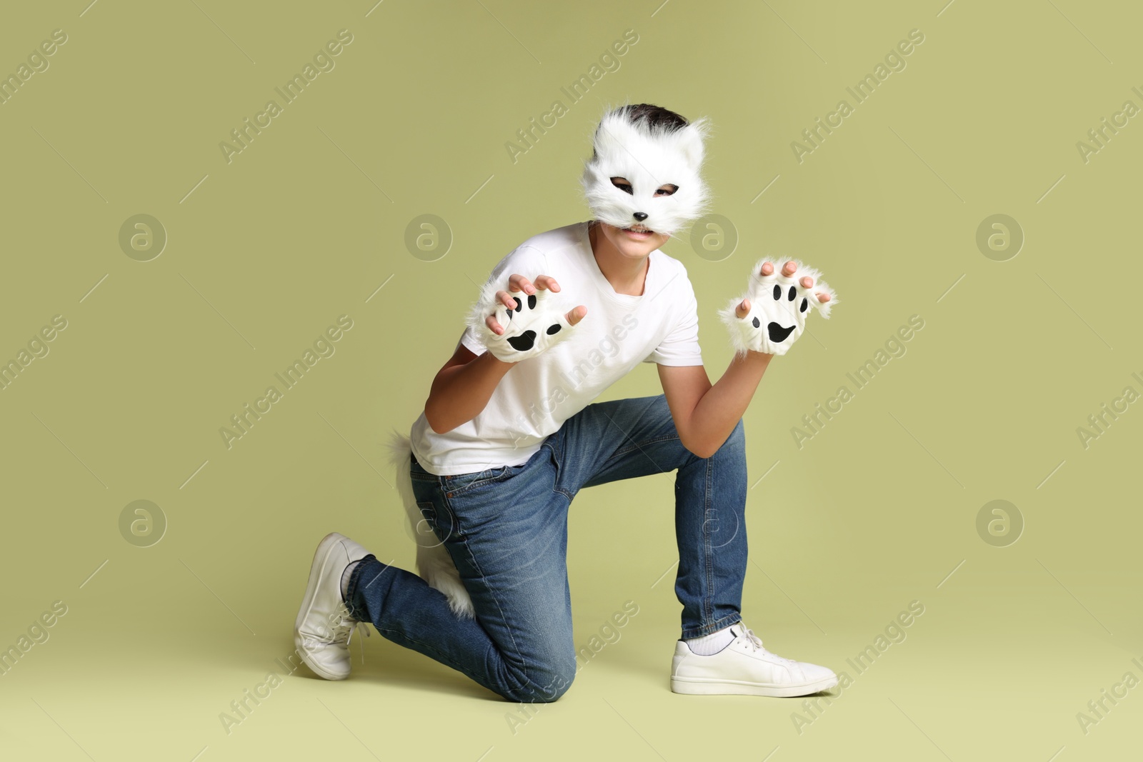 Photo of Quadrobics. Boy wearing cat mask, gloves and tail on pale olive background