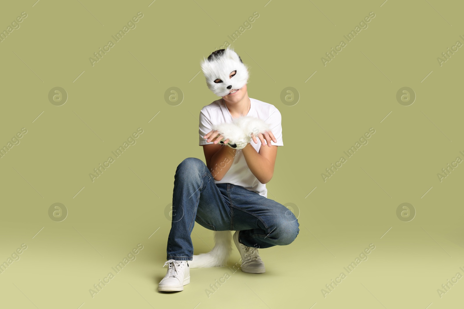 Photo of Quadrobics. Boy wearing cat mask, gloves and tail on pale olive background