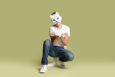 Photo of Quadrobics. Boy wearing cat mask, gloves and tail on pale olive background