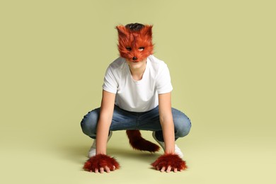 Photo of Quadrobics. Boy wearing fox mask, gloves and tail on pale olive background