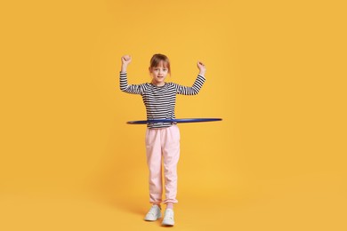 Photo of Cute little girl exercising with hula hoop on orange background