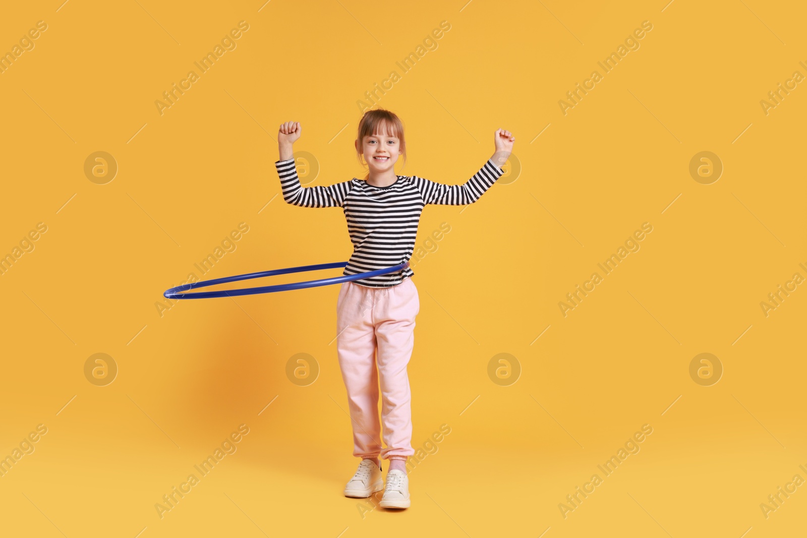 Photo of Cute little girl exercising with hula hoop on orange background