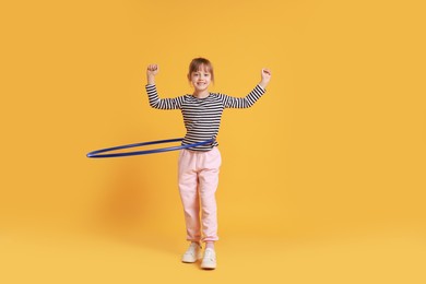 Photo of Cute little girl exercising with hula hoop on orange background