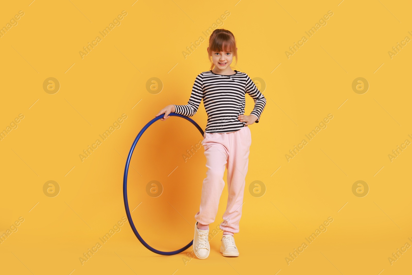 Photo of Cute little girl with hula hoop on orange background