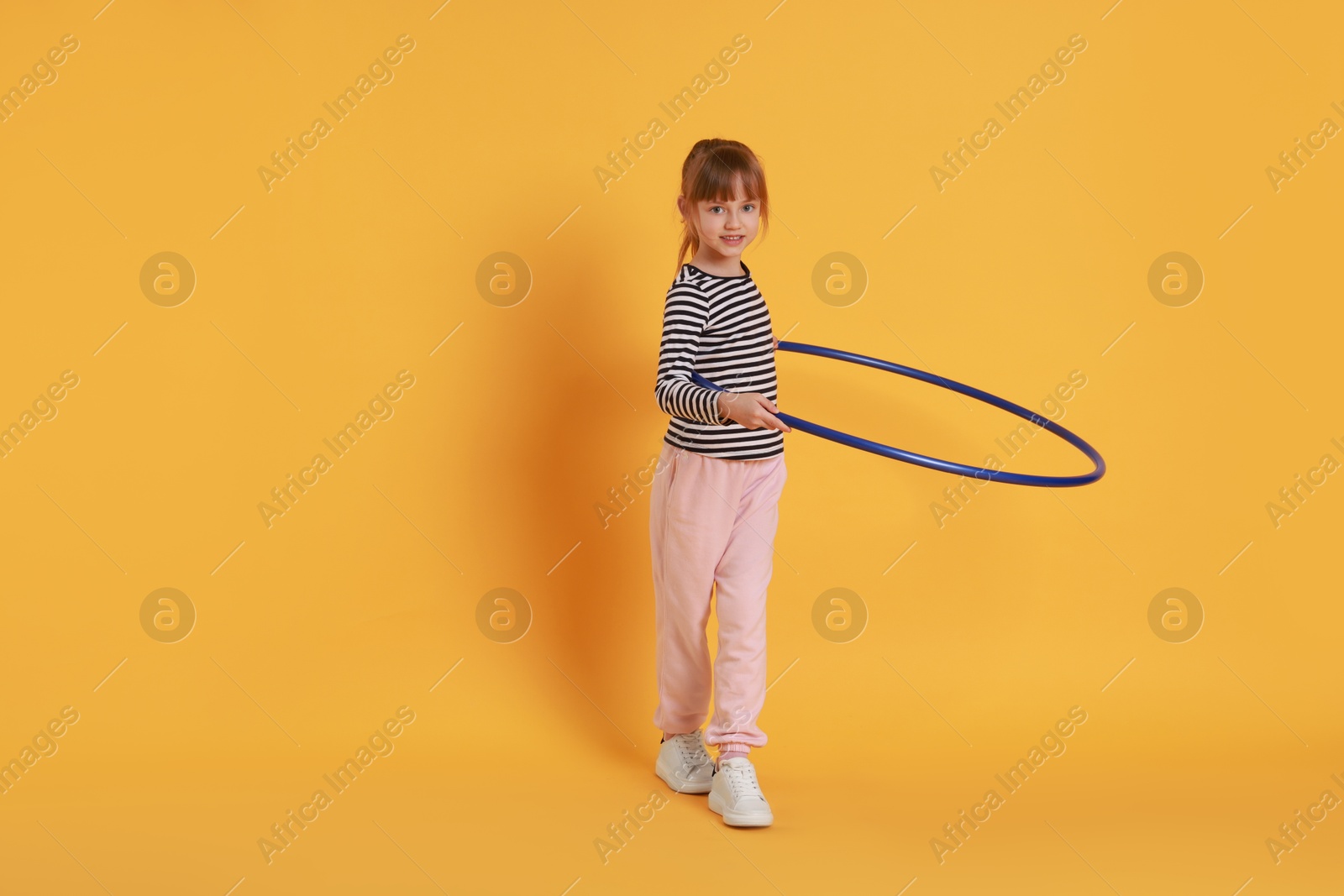 Photo of Cute little girl exercising with hula hoop on orange background