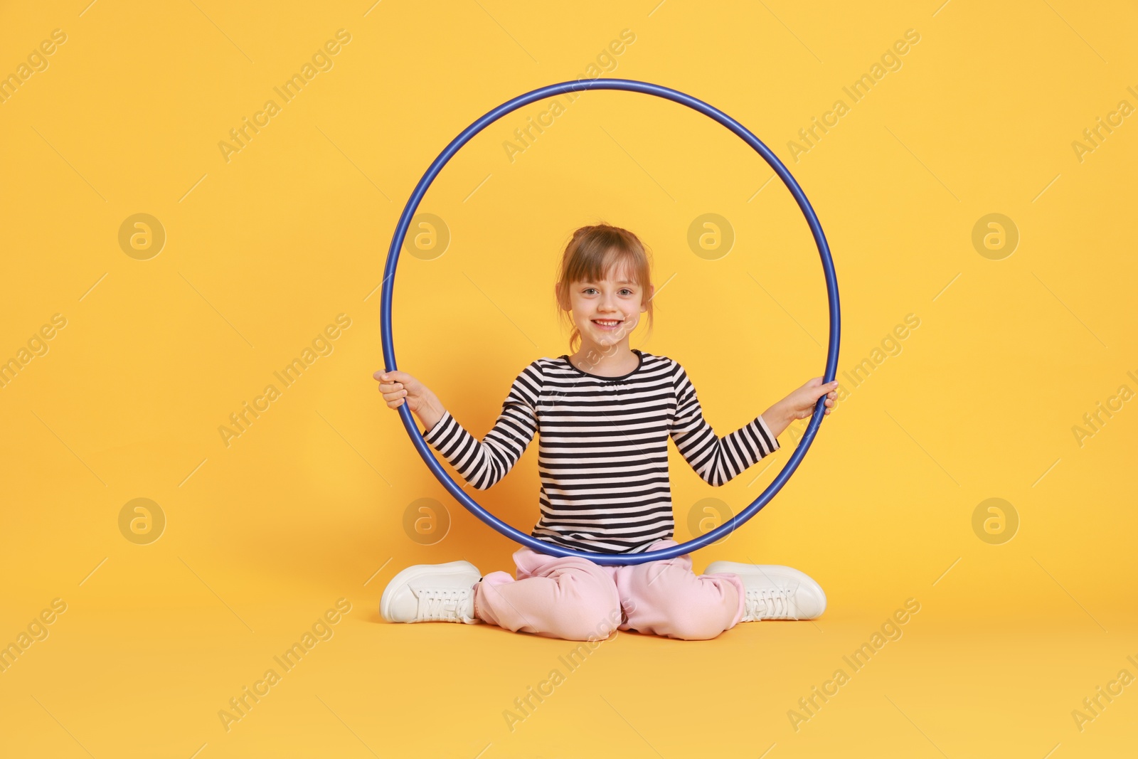 Photo of Cute little girl with hula hoop on orange background