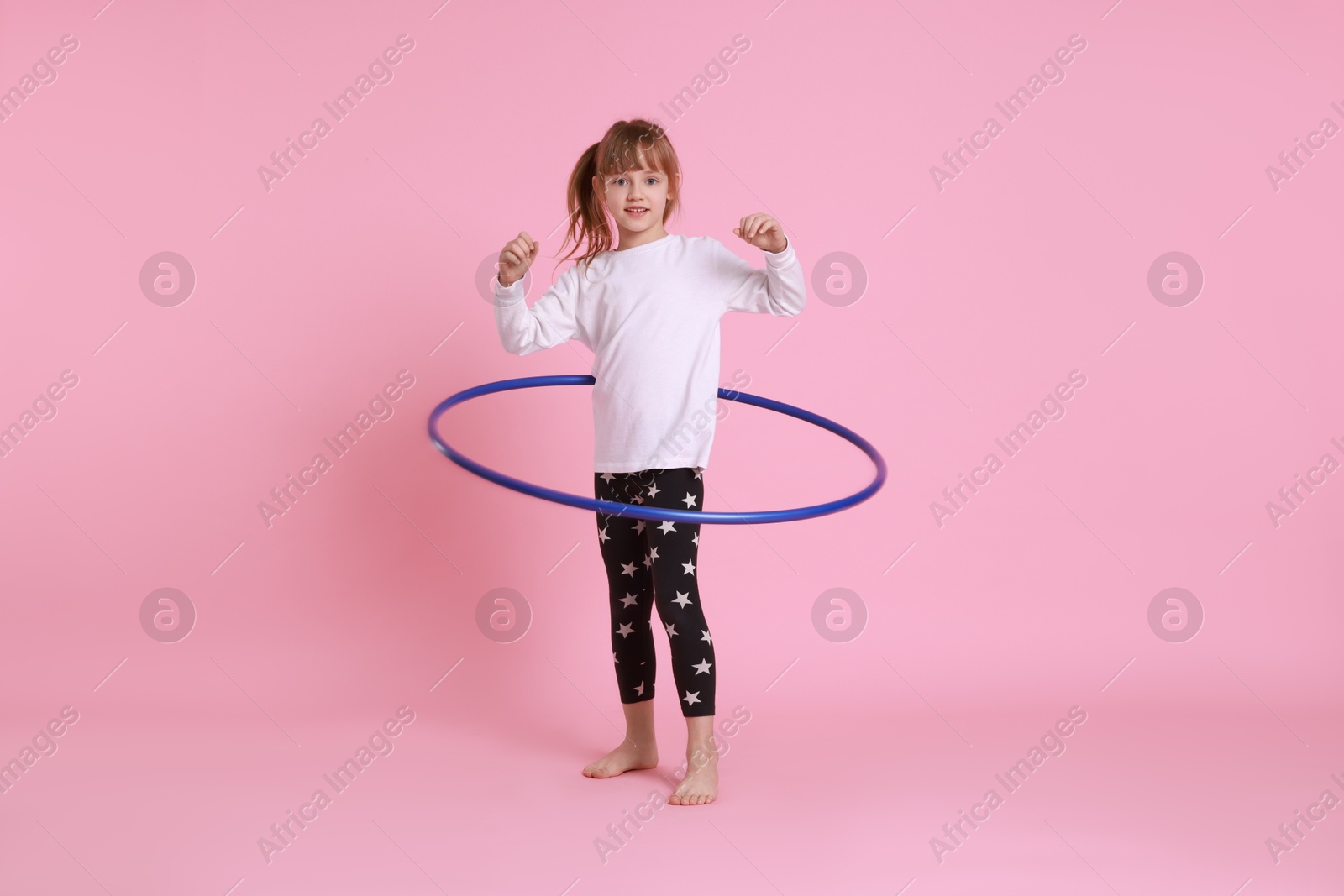 Photo of Cute little girl exercising with hula hoop on pink background