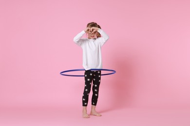 Photo of Cute little girl exercising with hula hoop on pink background