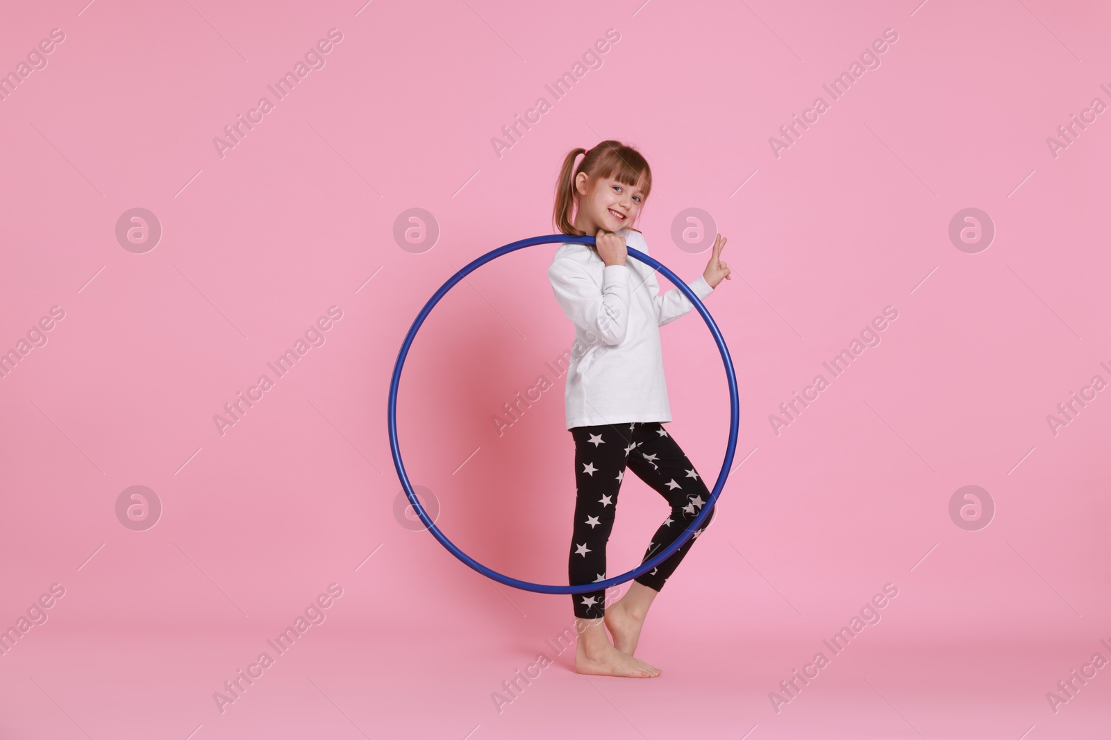 Photo of Cute little girl with hula hoop showing V-sign on pink background