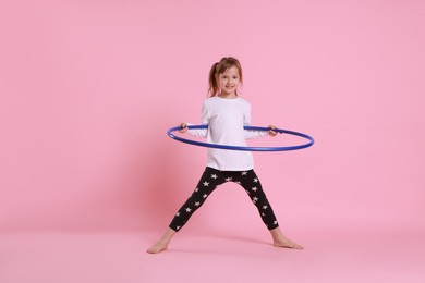 Photo of Cute little girl exercising with hula hoop on pink background