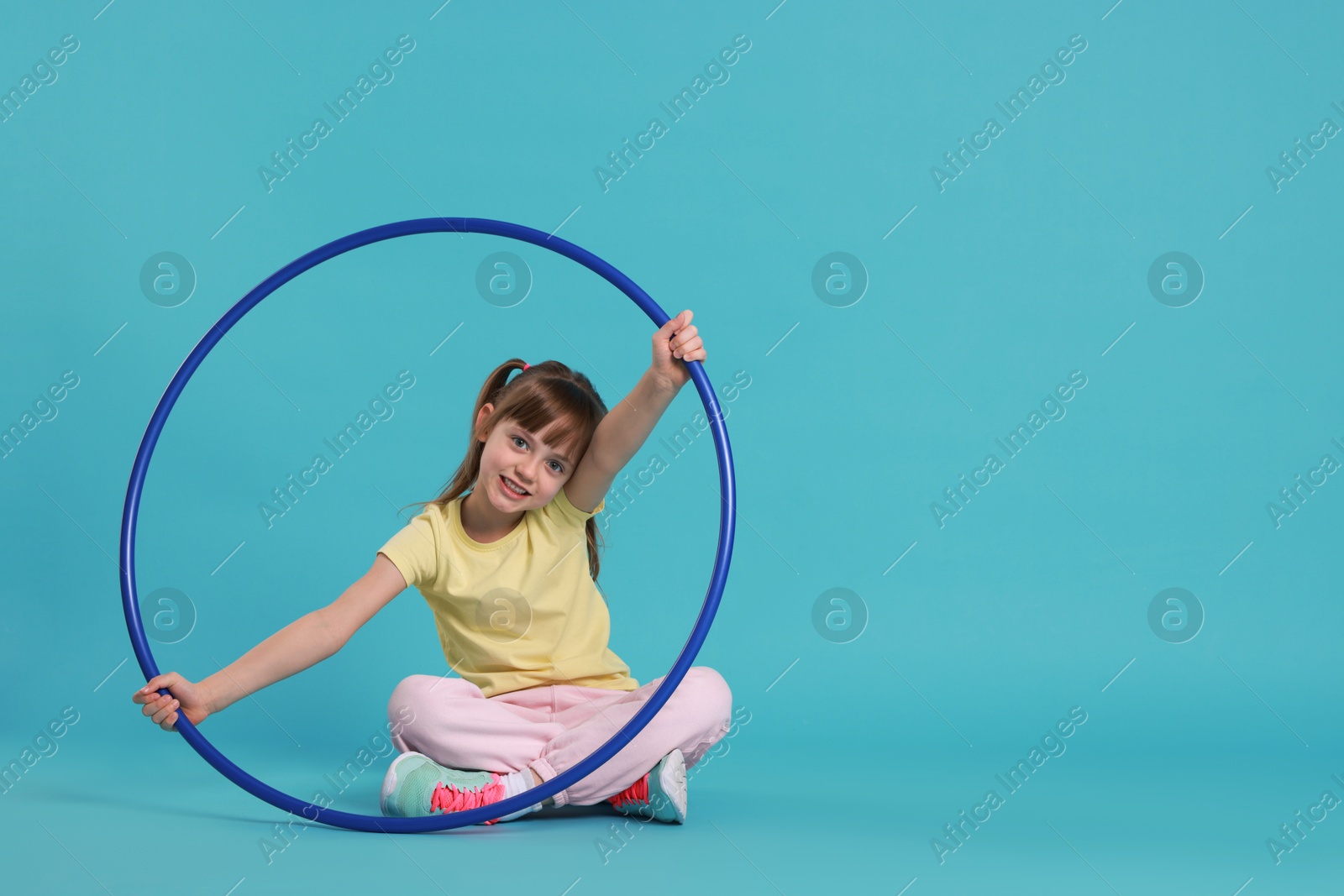 Photo of Cute little girl with hula hoop on light blue background, space for text