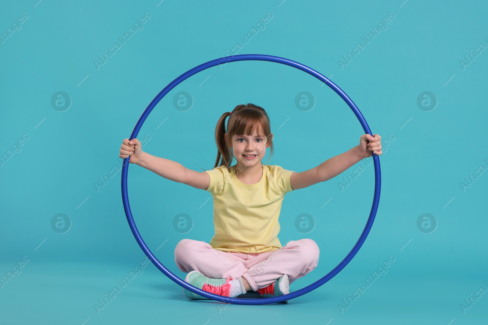 Photo of Cute little girl with hula hoop on light blue background