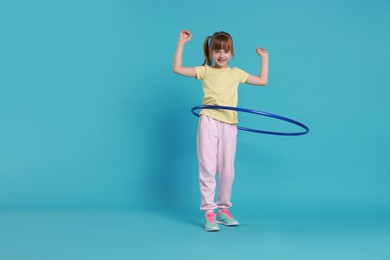 Photo of Cute little girl exercising with hula hoop on light blue background