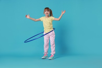 Photo of Cute little girl exercising with hula hoop on light blue background