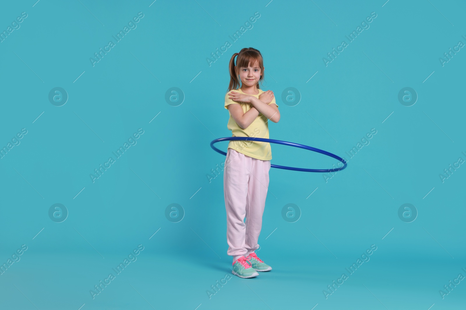 Photo of Cute little girl exercising with hula hoop on light blue background