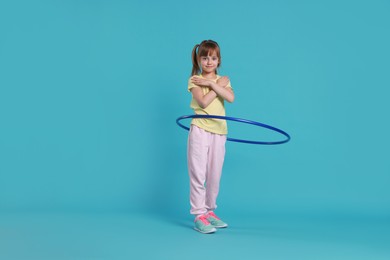 Photo of Cute little girl exercising with hula hoop on light blue background