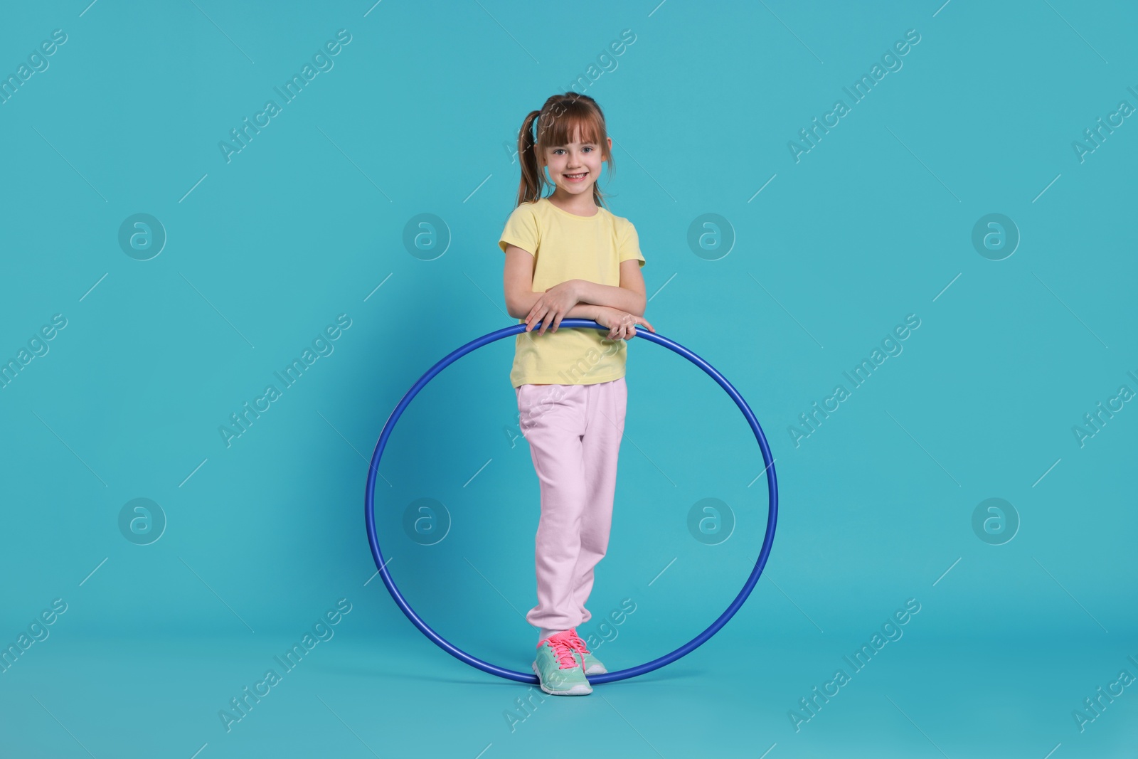 Photo of Cute little girl with hula hoop on light blue background