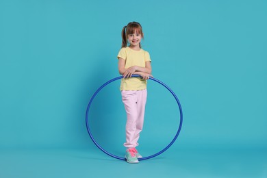 Photo of Cute little girl with hula hoop on light blue background