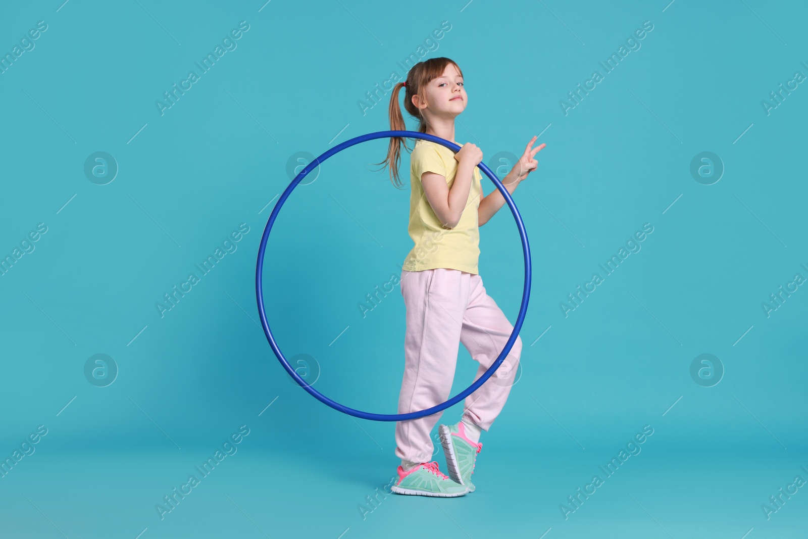 Photo of Cute little girl with hula hoop on light blue background