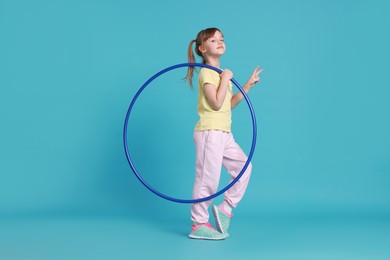 Photo of Cute little girl with hula hoop on light blue background