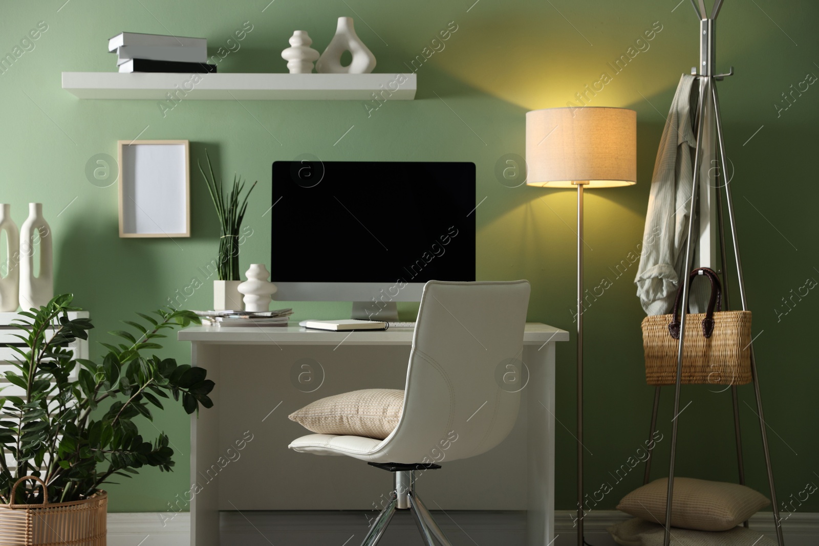 Photo of Home office. Comfortable workplace with desk, computer and lamp near light green wall in room