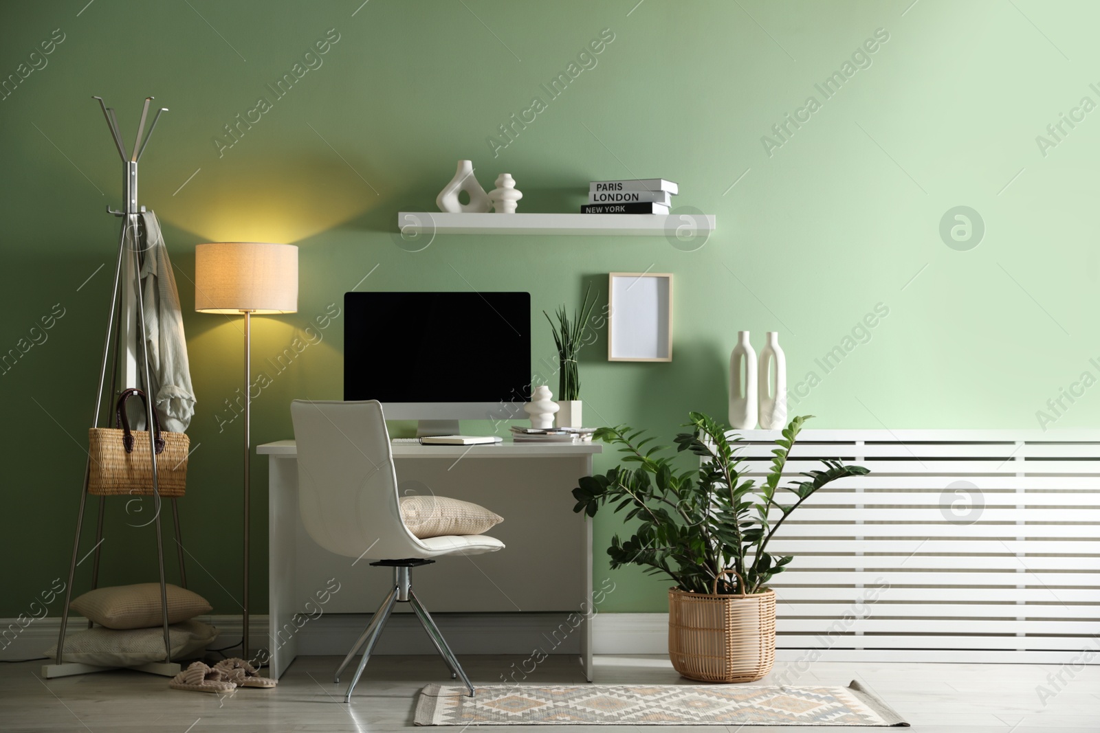 Photo of Home office. Comfortable workplace with desk, computer and lamp near light green wall in room