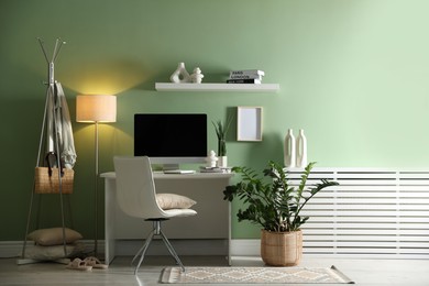 Photo of Home office. Comfortable workplace with desk, computer and lamp near light green wall in room