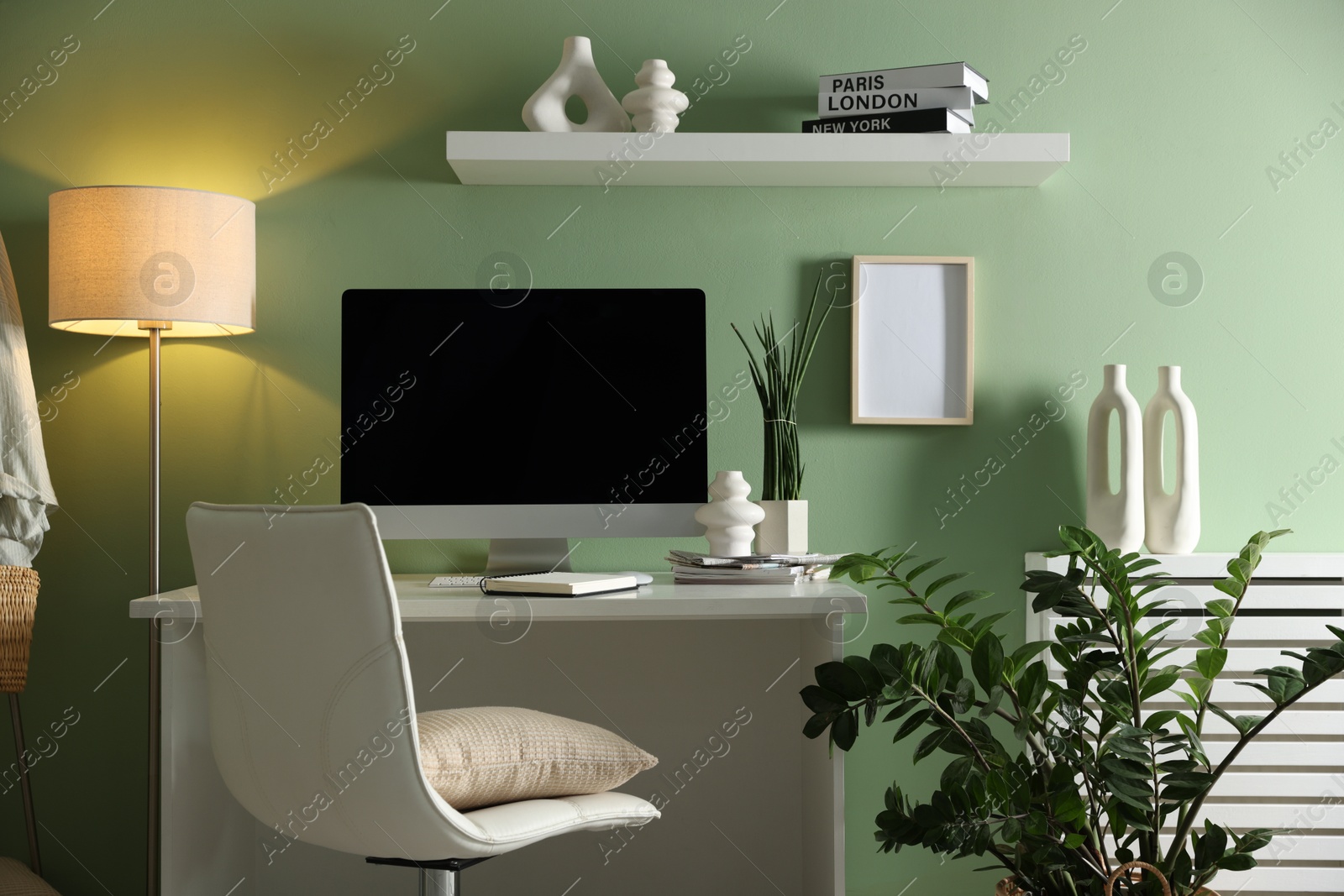 Photo of Home office. Comfortable workplace with desk, computer and lamp near light green wall in room