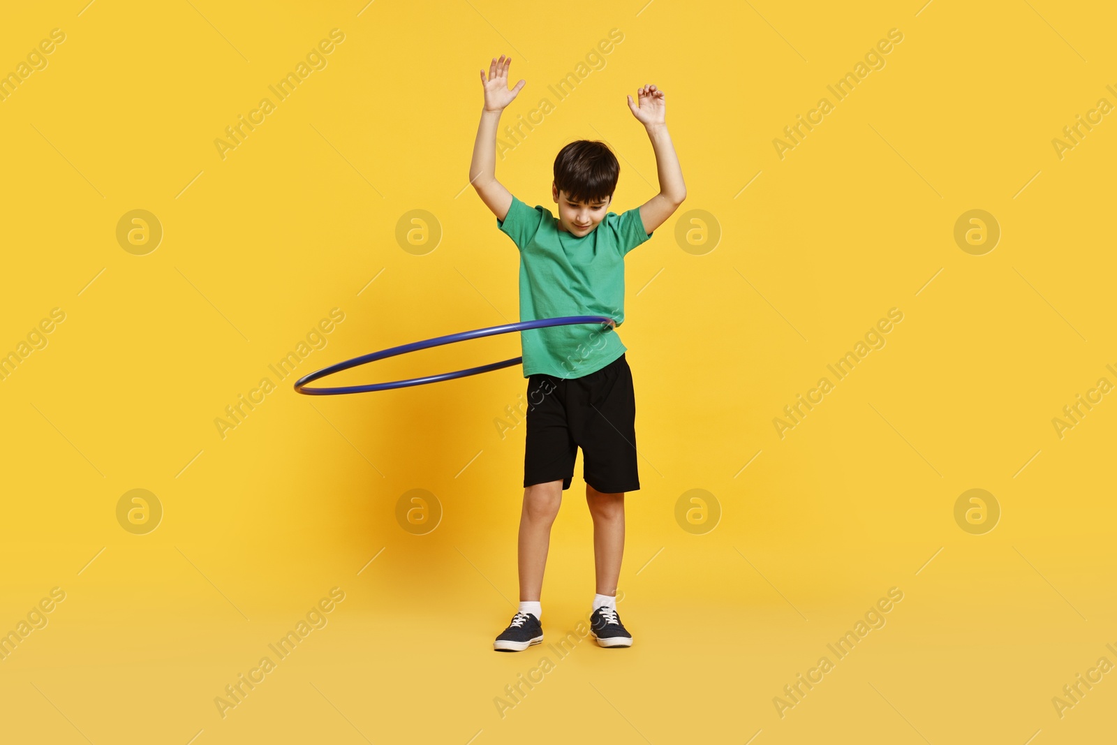 Photo of Boy exercising with hula hoop on yellow background