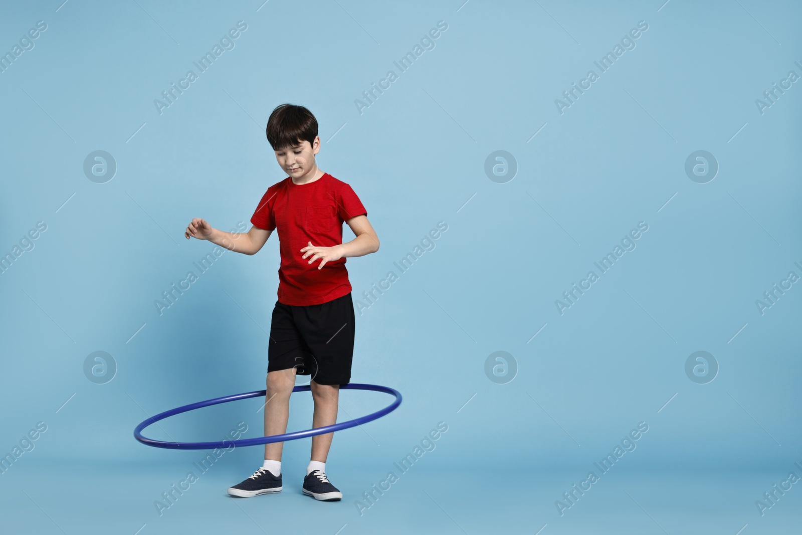 Photo of Boy exercising with hula hoop on light blue background, space for text