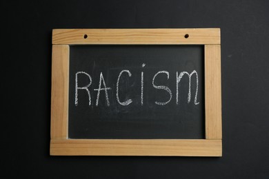 Photo of Chalkboard with word Racism on black background, top view