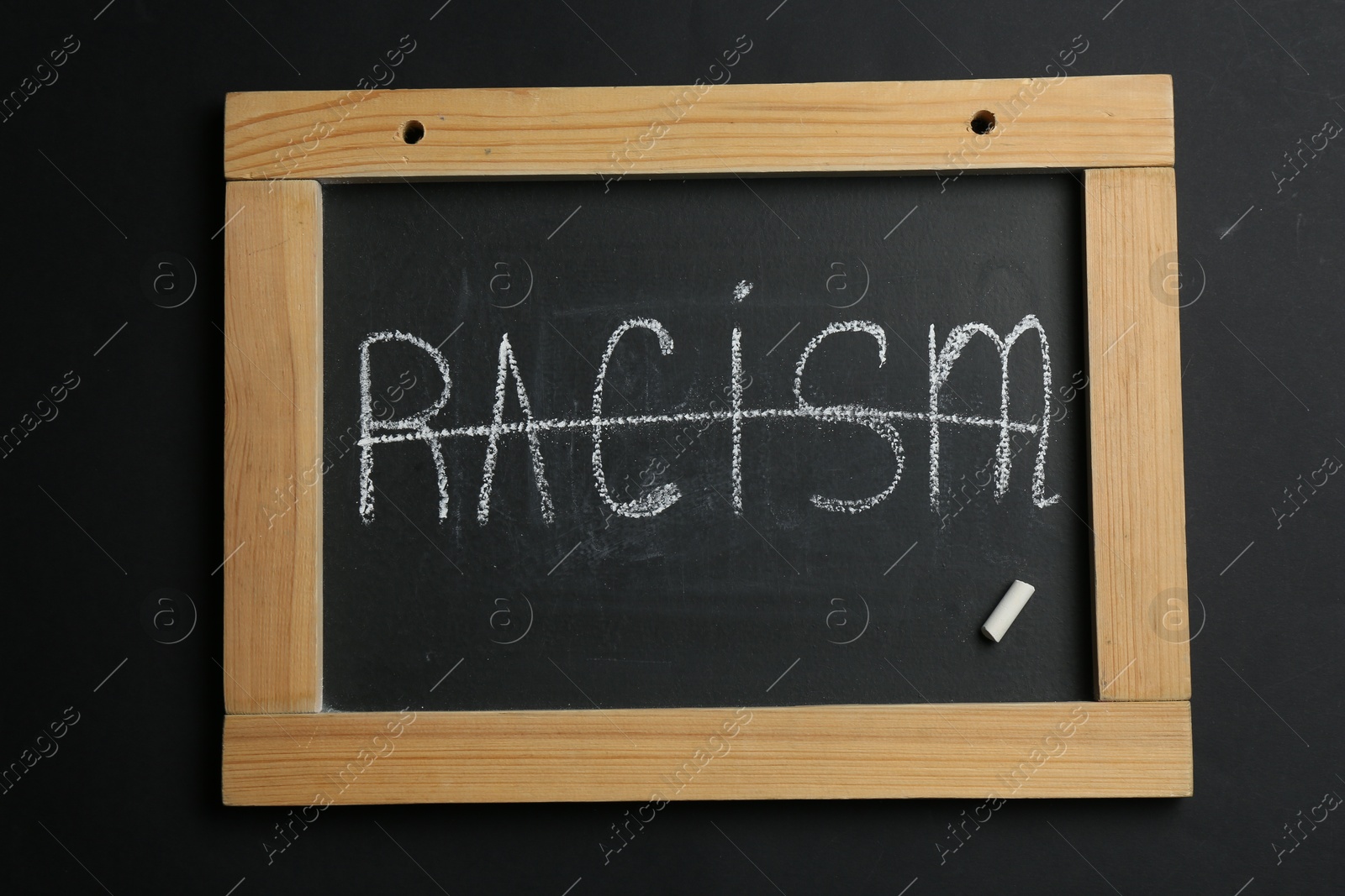 Photo of Chalkboard with word Racism on black background, top view