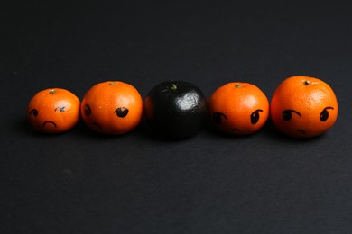 Photo of Stop racism. One black tangerine among orange ones on black background, closeup