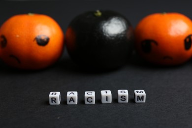 Photo of One black tangerine among orange ones and word Racism made with beads on black background, closeup