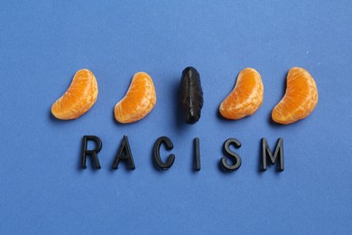 Photo of Word Racism and tangerine segments of different colors on blue background, flat lay