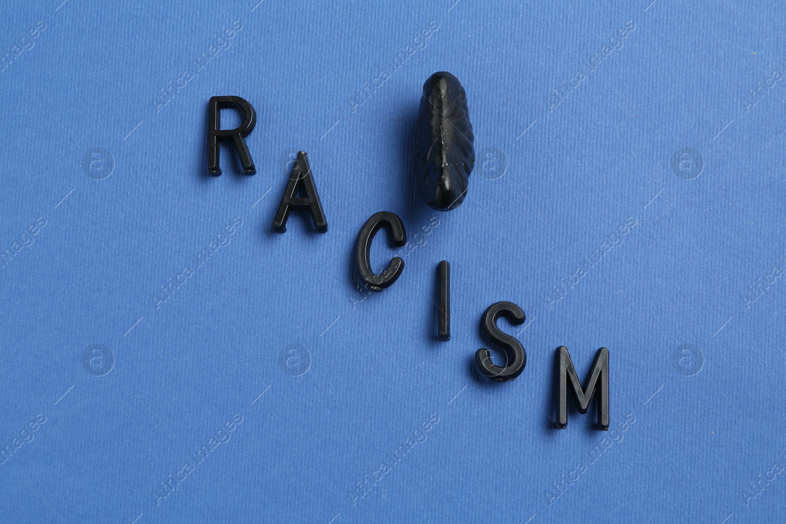 Photo of Word Racism and black tangerine segment on blue background, top view