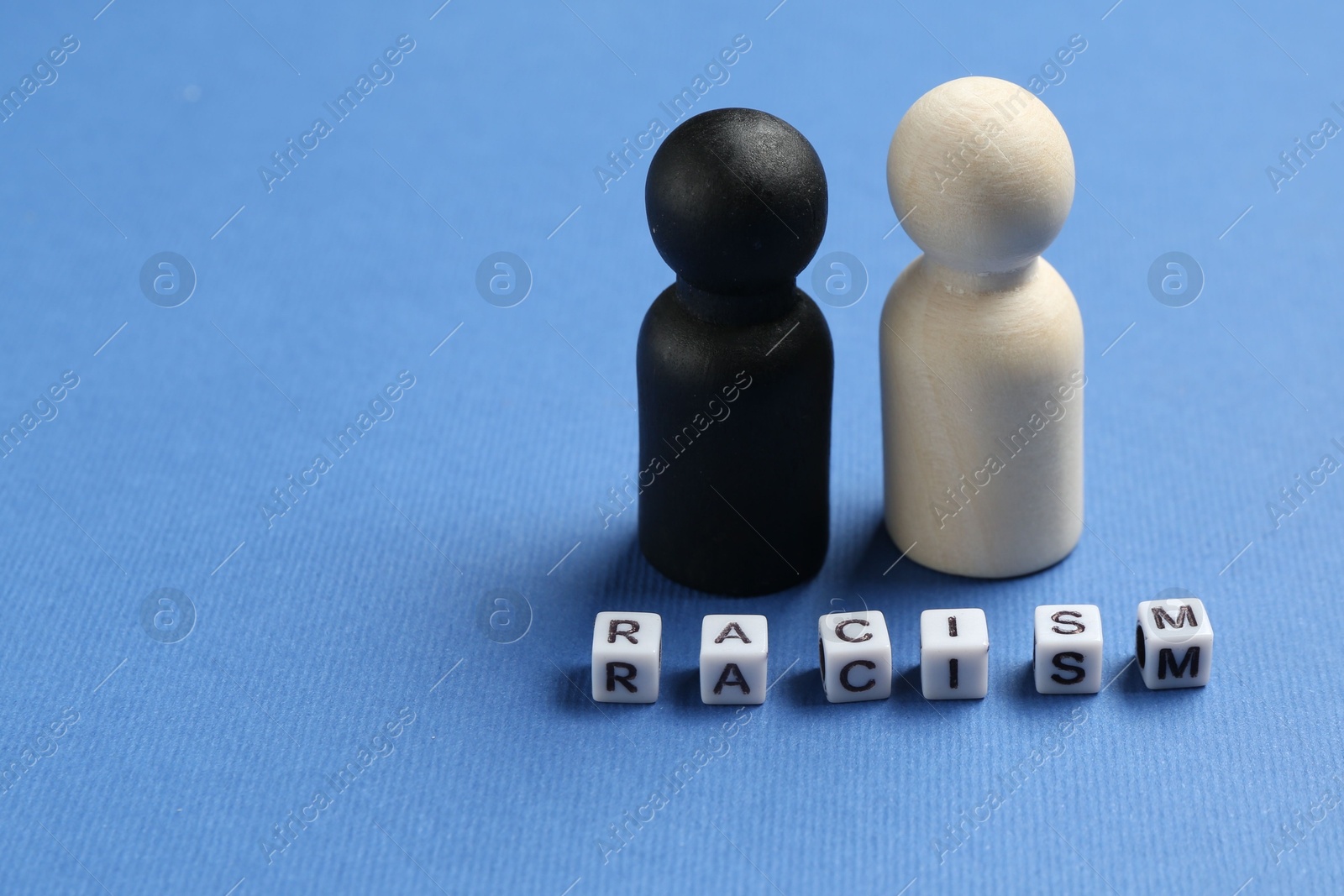 Photo of Word Racism and human figures of different colors on blue background, closeup