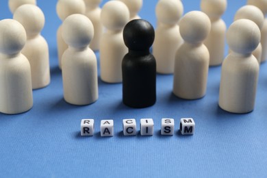 Photo of Word Racism and human figures of different colors on blue background, closeup