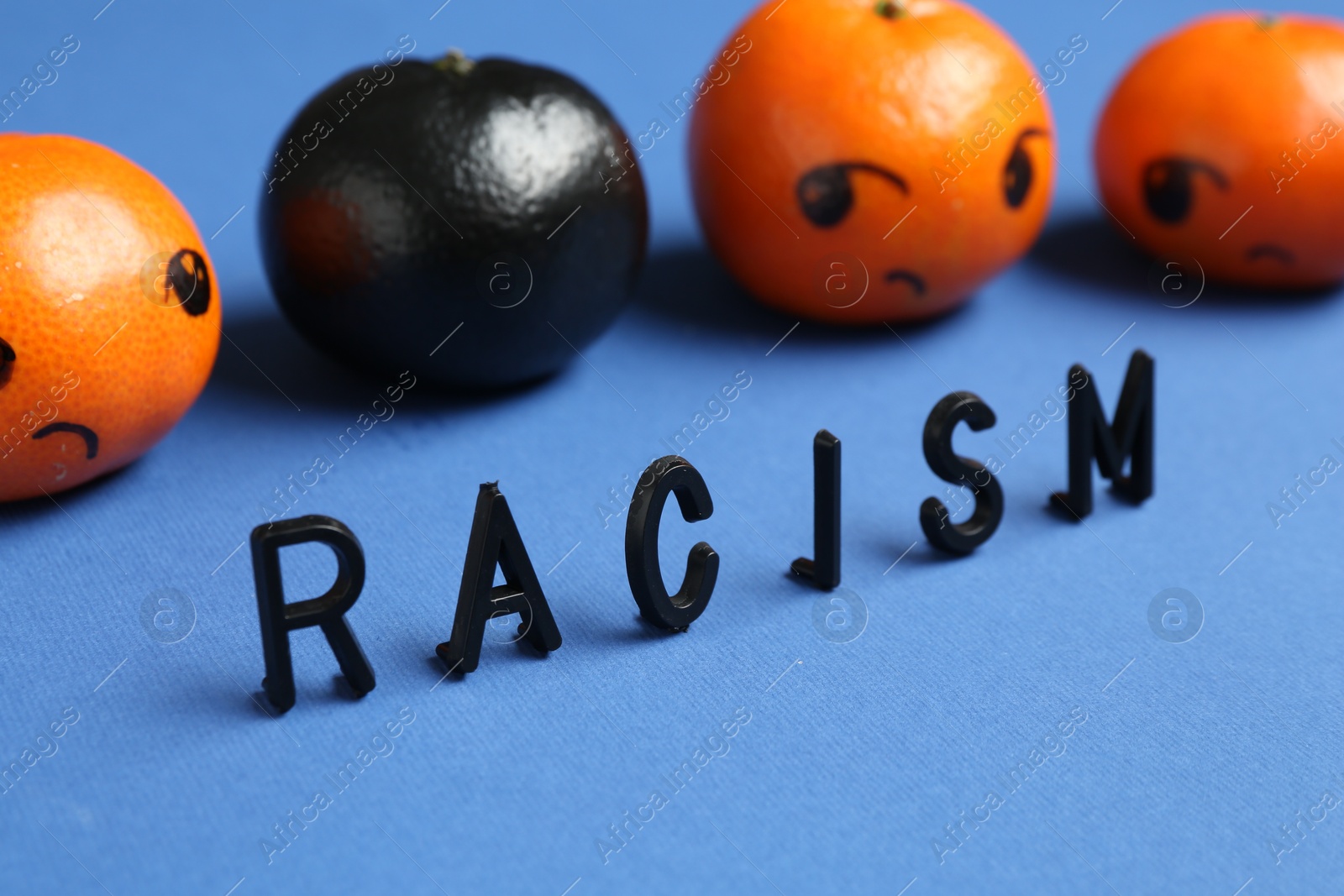 Photo of One black tangerine among orange ones and word Racism made with beads on blue background, closeup