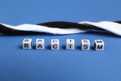 Photo of Word Racism and intertwined shoelaces of different colors on blue background, closeup