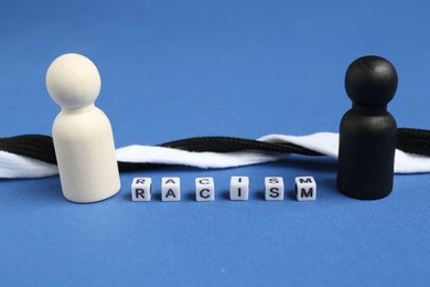 Photo of Word Racism, human figures and intertwined shoelaces of different colors on blue background, closeup