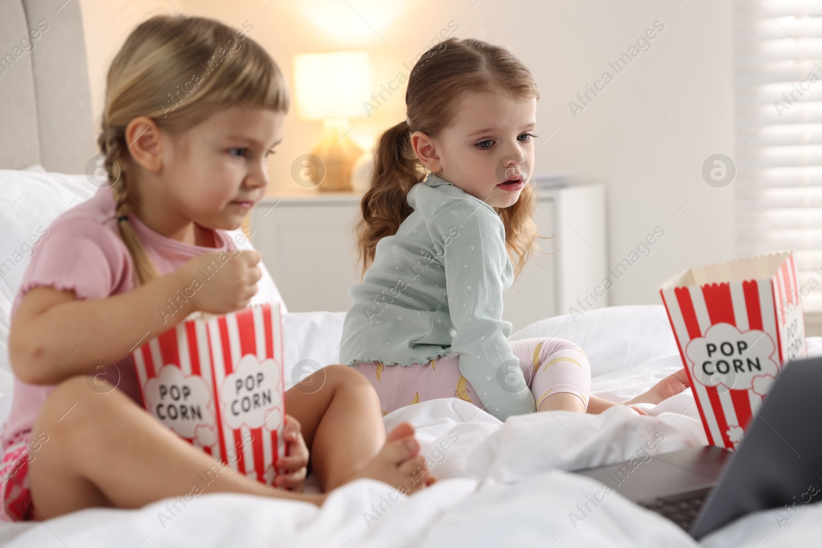 Photo of Cute little sisters with popcorn buckets watching something on laptop at home, selective focus